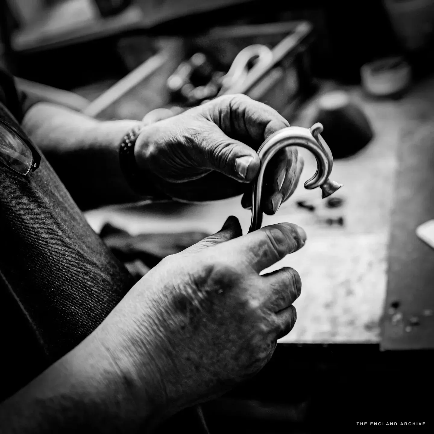 Two hands inspecting an ornate cast and scrolled silver handle at a bench.
