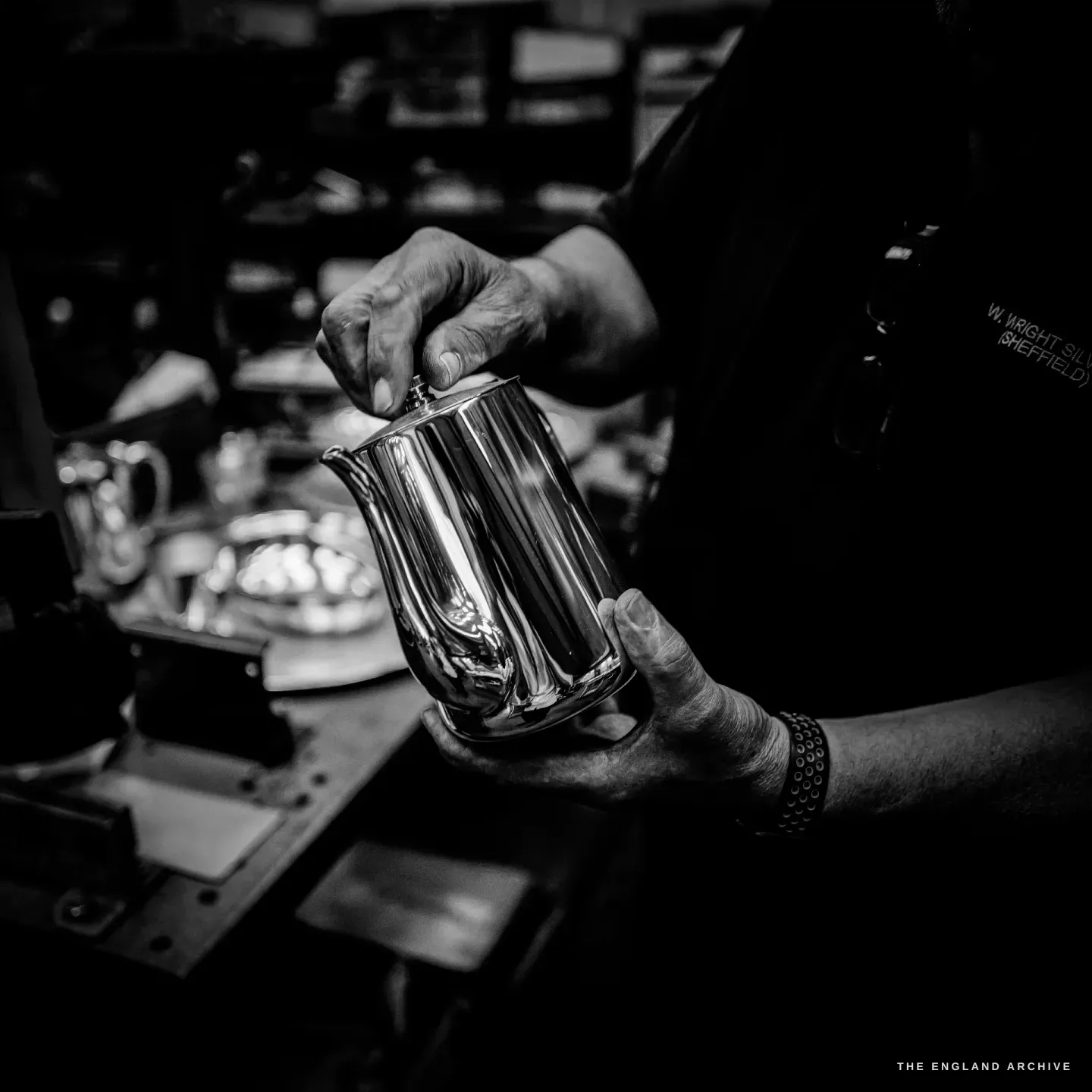 Stephen Wright’s hands cradling a finished mirror-polished silver milk jug, the bright silver glowing against his dark shirt.