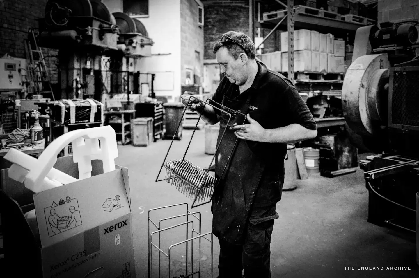 A worker in an apron loading cutlery into a wire dipping rack at the plating bench.