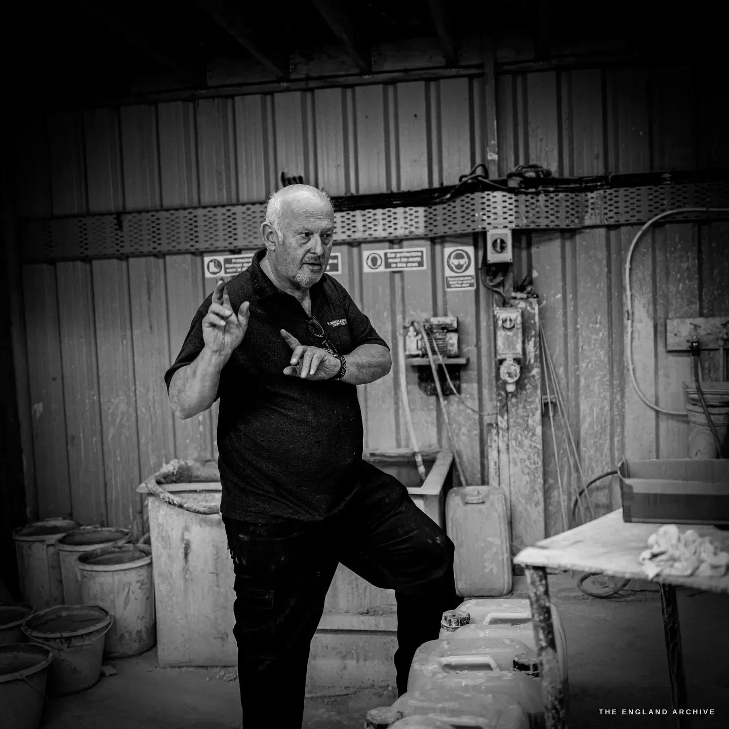 Stephen Wright in the plating room mid-explanation, both hands raised, one foot up on a drum, caught full of energy.