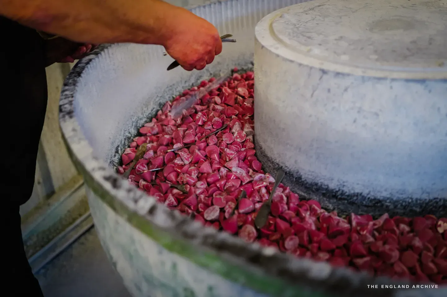 A hand lowering forks into a vibratory finishing bowl heaped with bright magenta ceramic media stones.