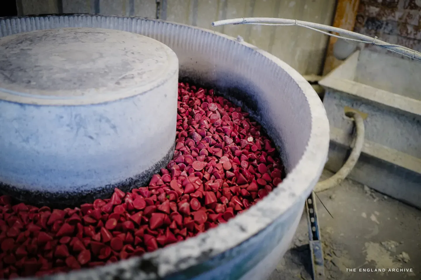 A close view of the vibratory finisher bowl heaped with crimson ceramic media stones around a grey central column.