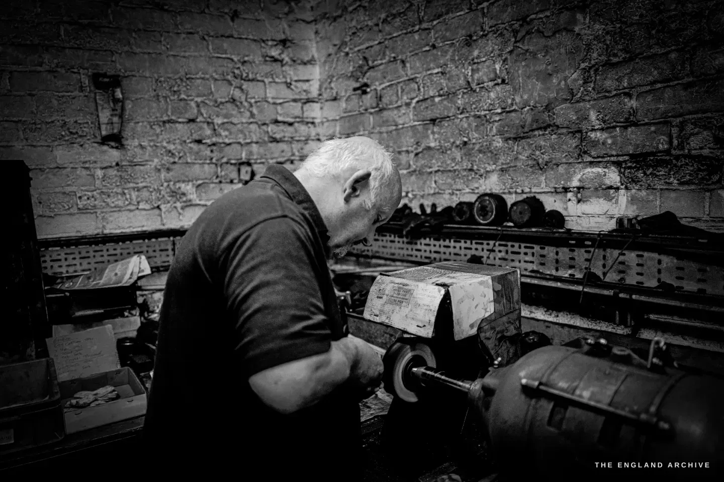 Stephen Wright bent over a polishing lathe, working a piece against the mop, a brick wall behind.