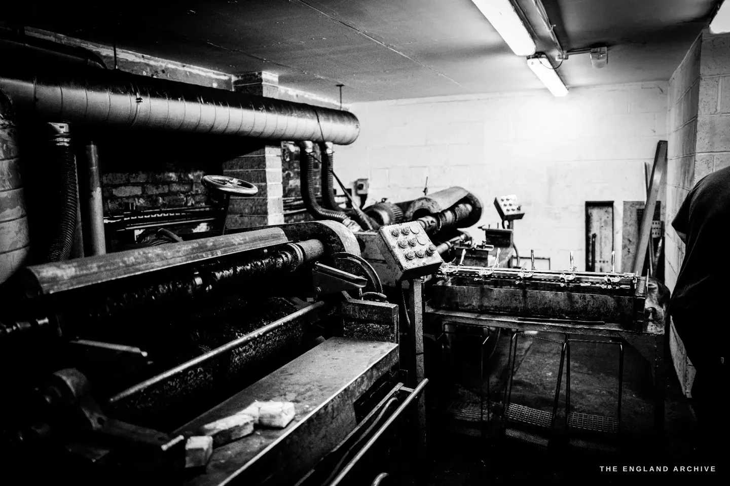 A pair of heavy rolling mills with thick steel rollers and overhead ducting, used to roll metal stock down to gauge.