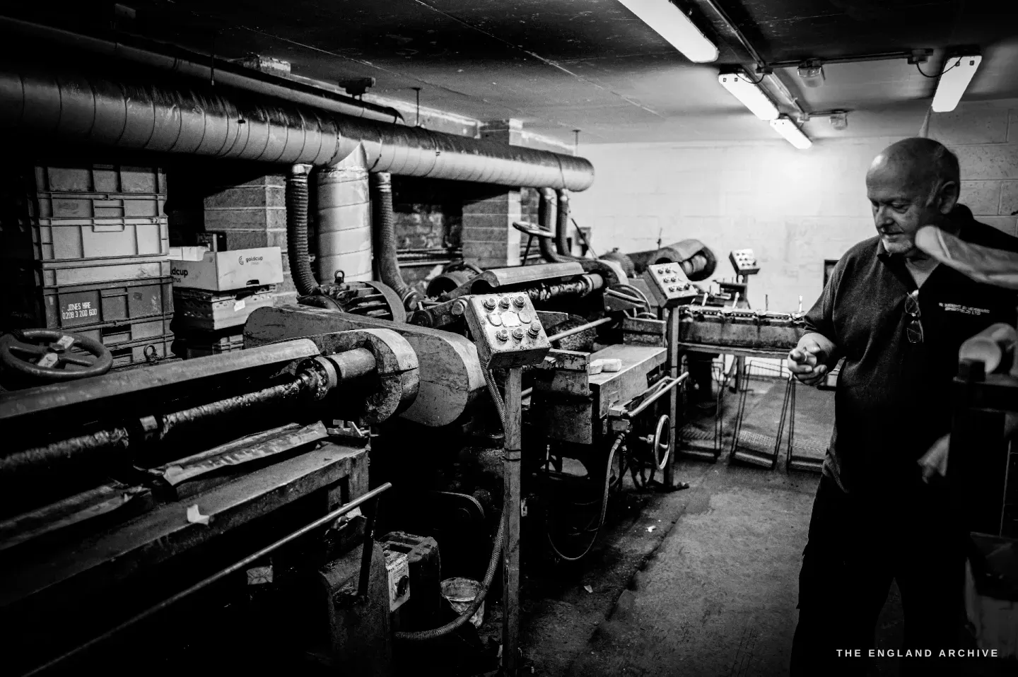 Stephen Wright reaching to the controls of the rolling mills, a strip of metal stock to hand.