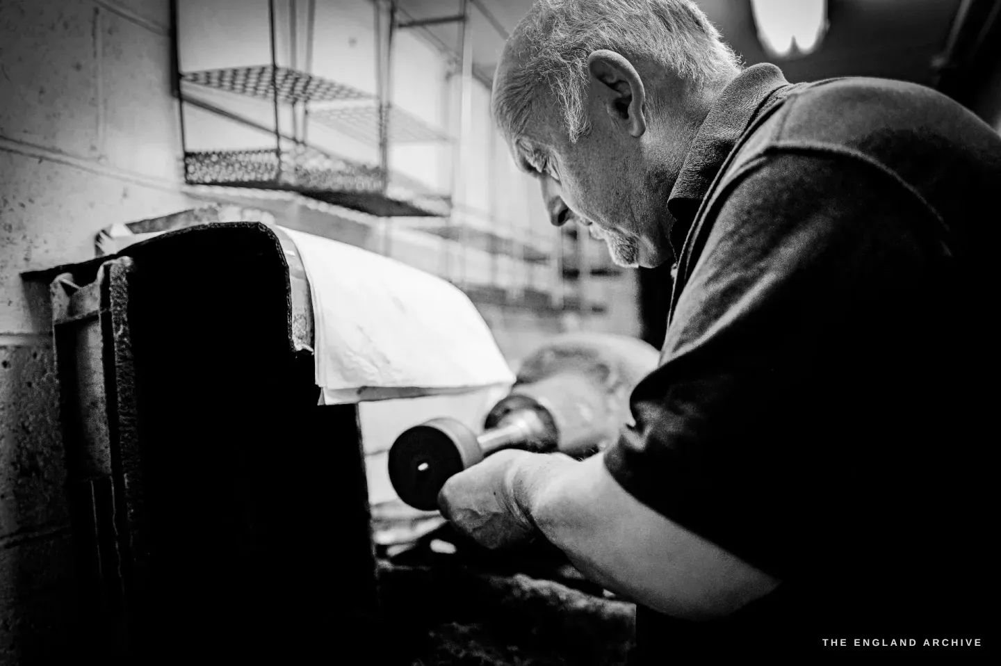 A close profile of Stephen Wright bent over a buffing spindle, concentrating, holding a piece to the mop.