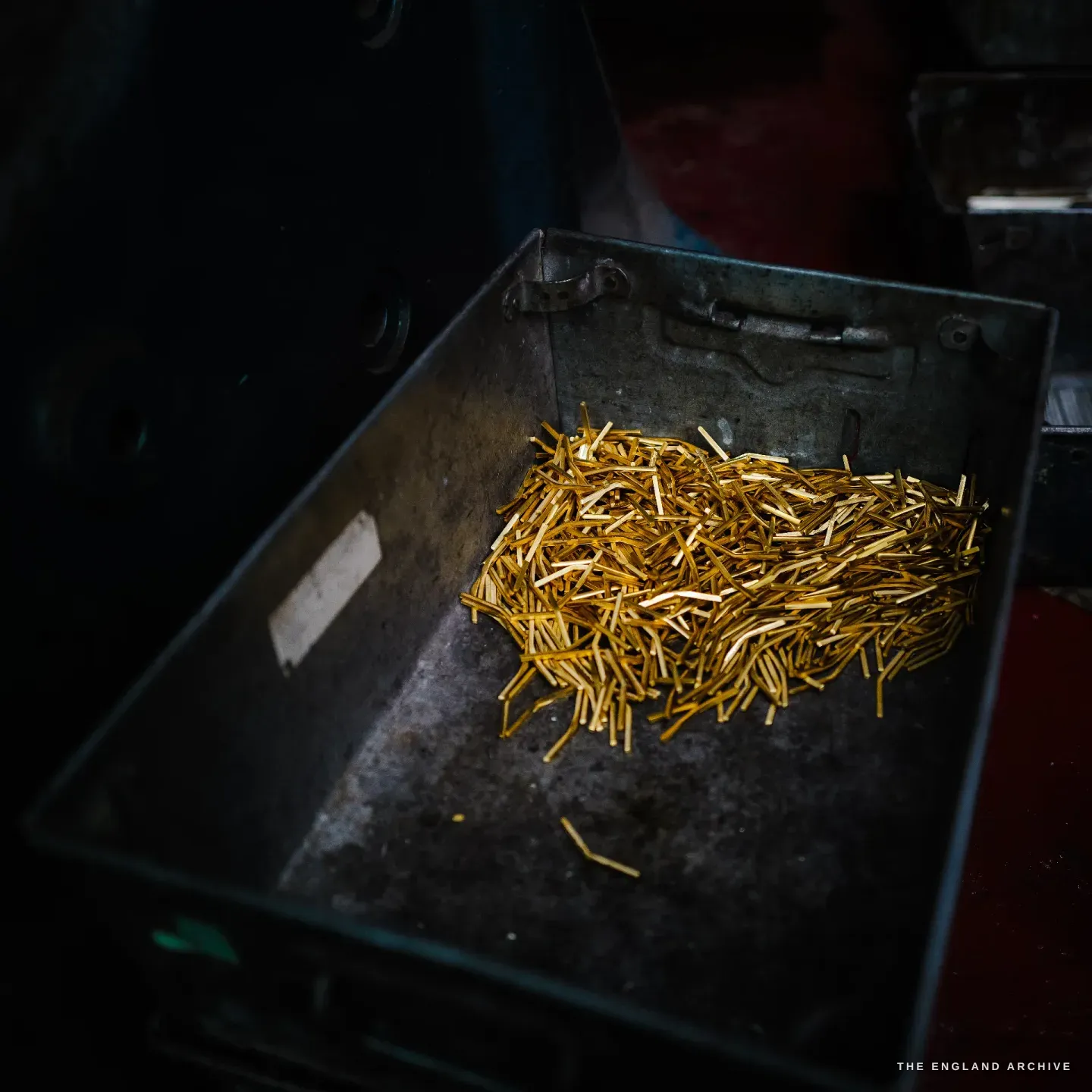 A steel crate holding a glowing pile of slim golden brass offcuts.