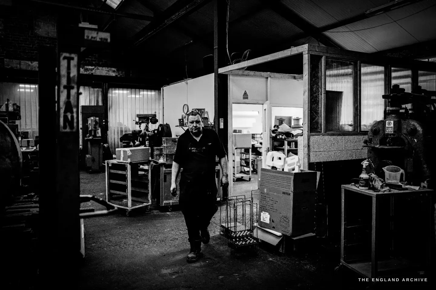 A wide view down the workshop floor, Stephen Wright walking toward the camera between the benches and machines.