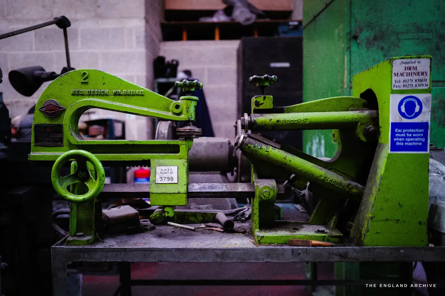 A bright green fly press numbered 2 on a steel bench, with a handwheel, a DRM Machinery supplier label and a safety notice.