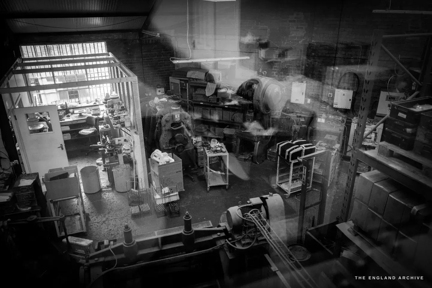An elevated wide view across the whole workshop floor, benches, machines and a worker below.