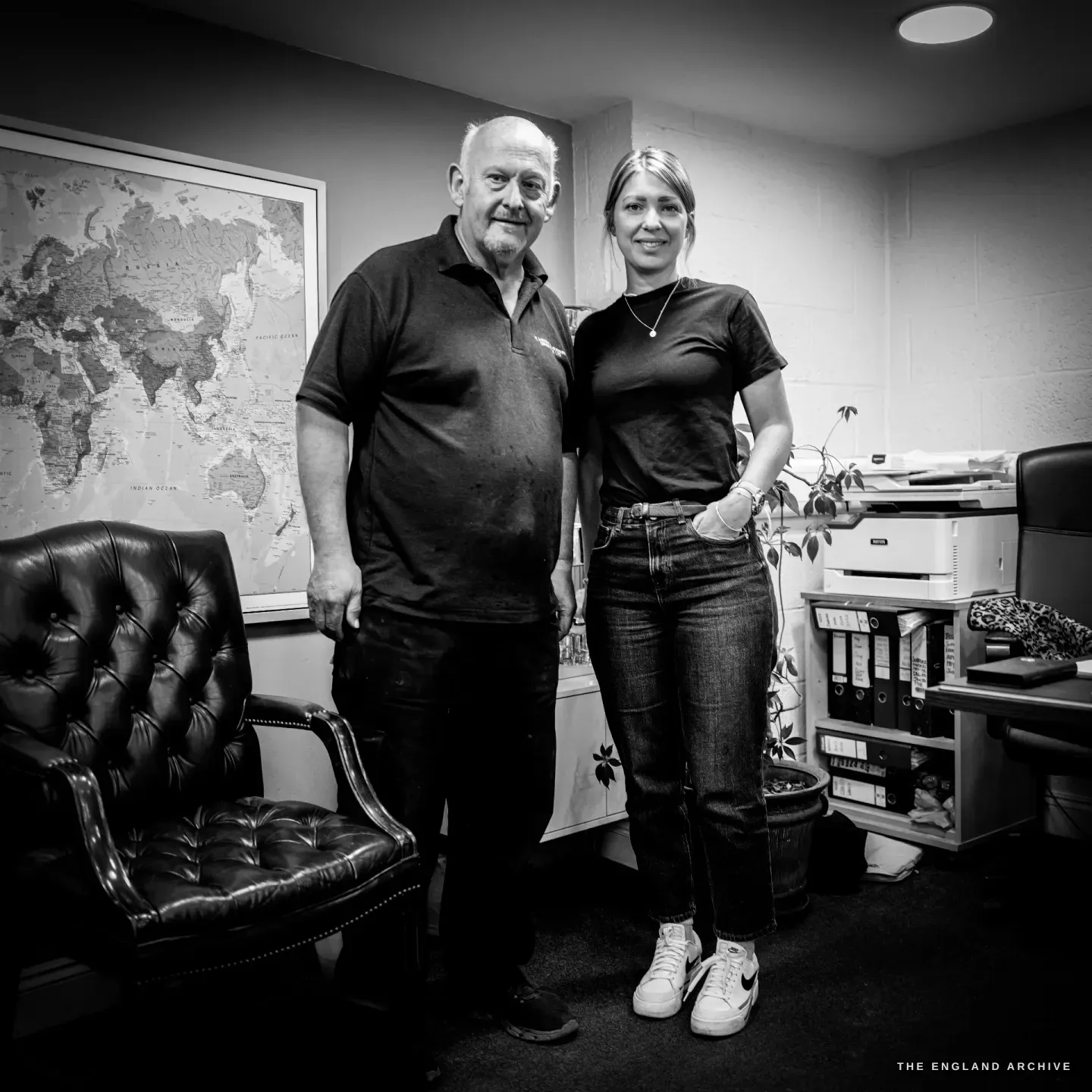 Stephen Wright and his daughter Samantha standing together in the office, a framed world map and a leather chair behind them.