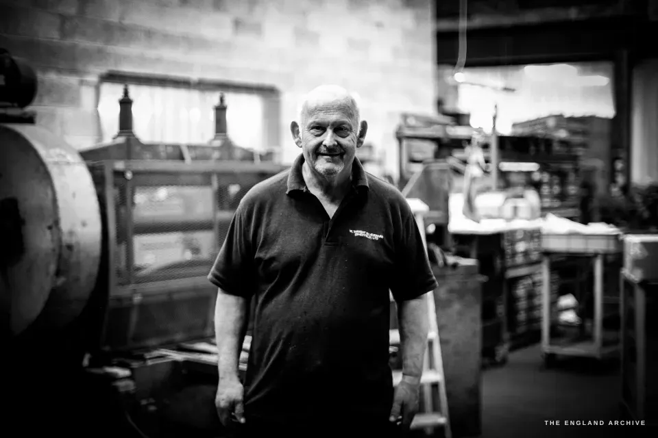 Stephen Wright standing in the middle of his workshop, hands in his pockets, smiling, drop-stamp presses and benches flanking him.