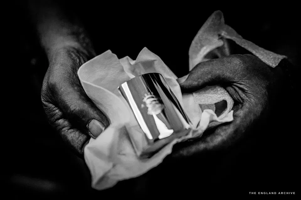 Stephen Wright’s hands cradling a small polished silver piece in tissue paper, finishing it.