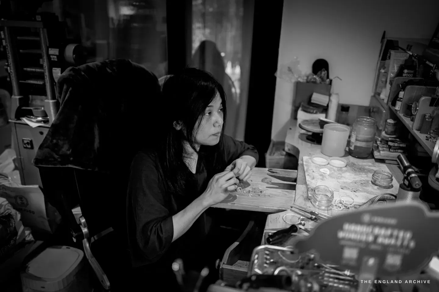 A wider view of Yuyi talking at the bench, shelves of jars and chemicals behind her.