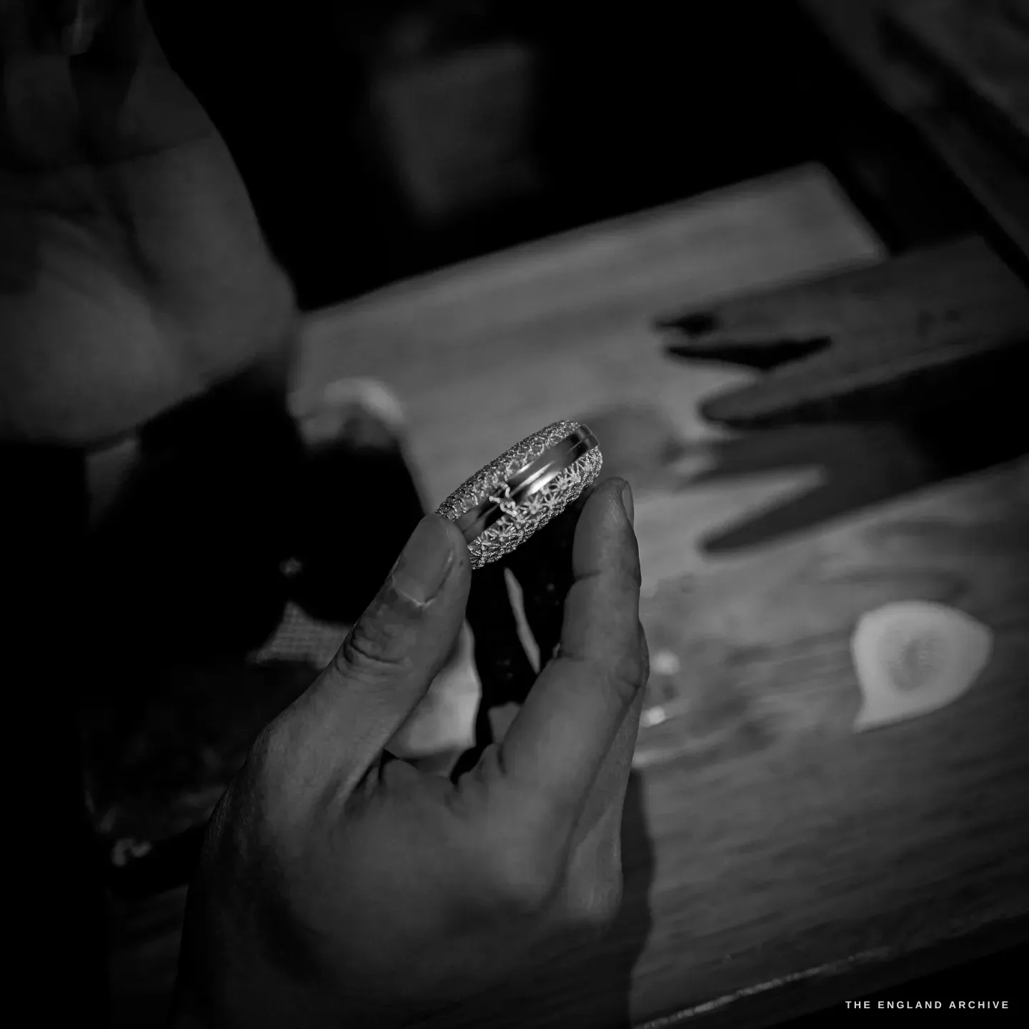 A hand holds a filigree band ring edge-on to the light, the star-pattern openwork showing through.