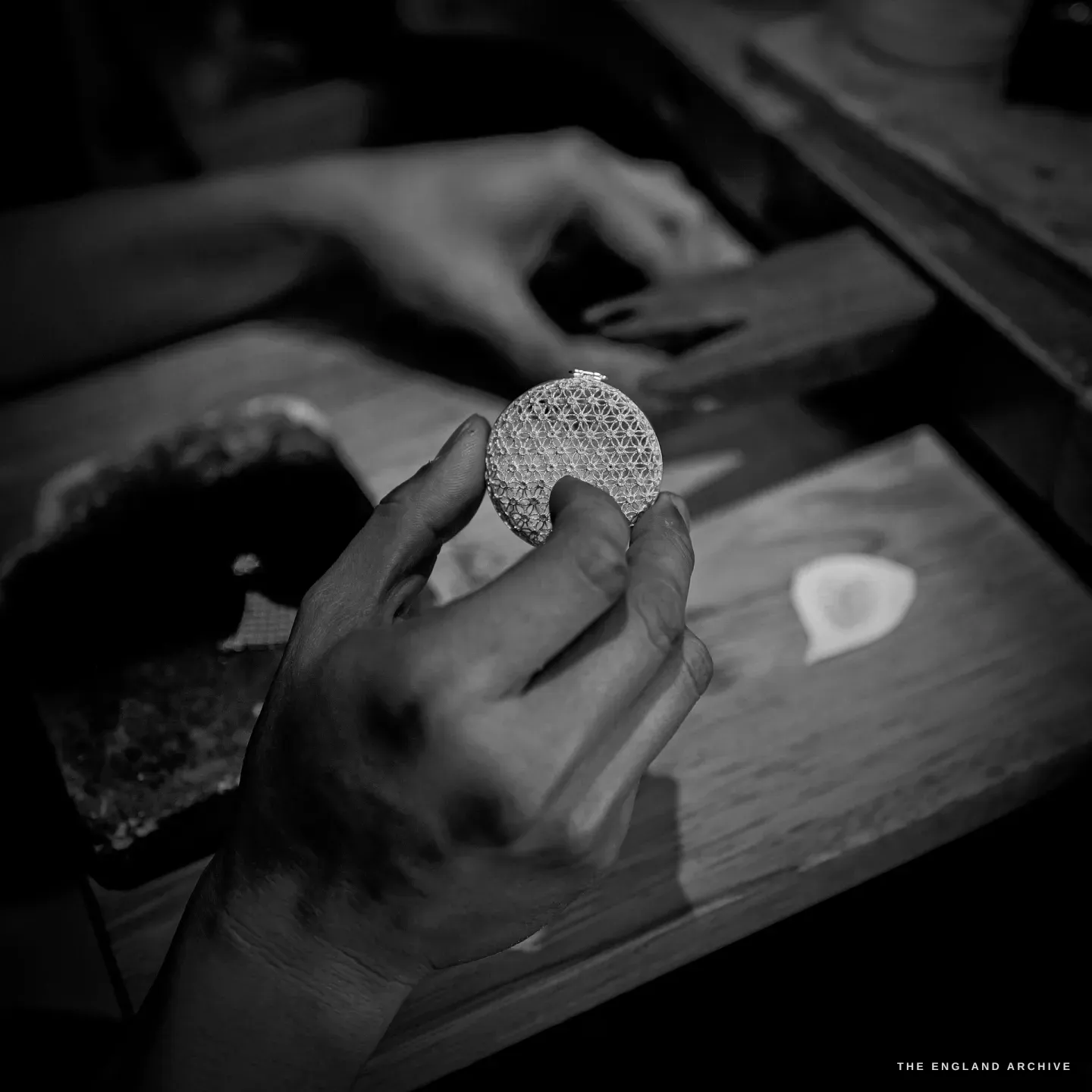 A hand holds a round openwork filigree disc up to the light, a geometric star lattice of fine silver wire.