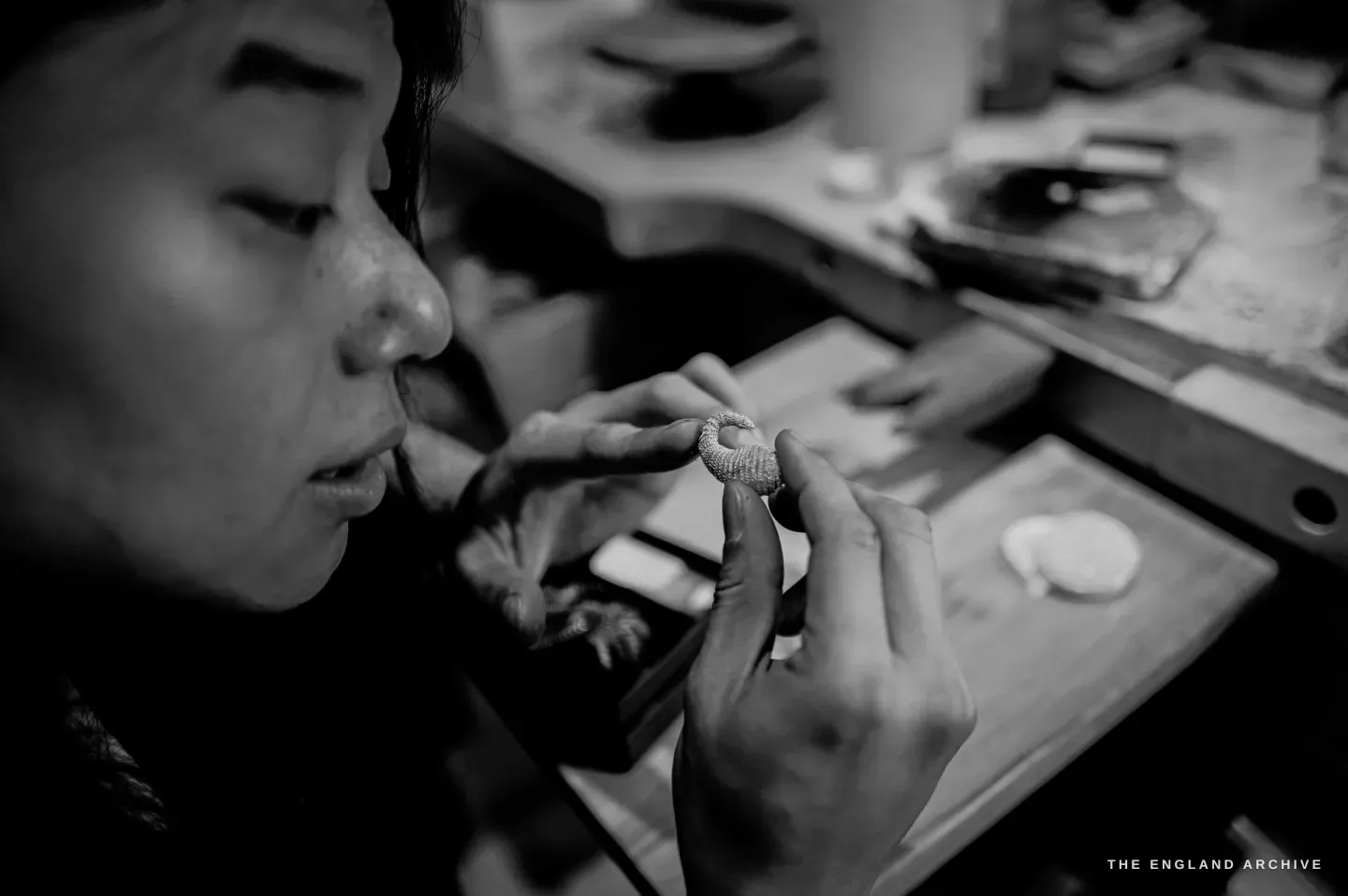 A tight profile of Yuyi’s face, lips parted in concentration, inspecting a textured openwork ring held between her fingers.