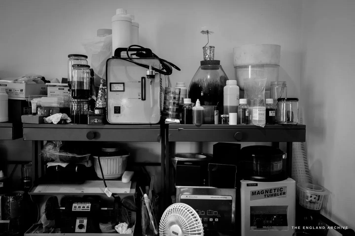 The finishing shelf: jars and dropper bottles, an electrolytic plating unit with a gauge, an ultrasonic cleaner and a magnetic tumbler below.