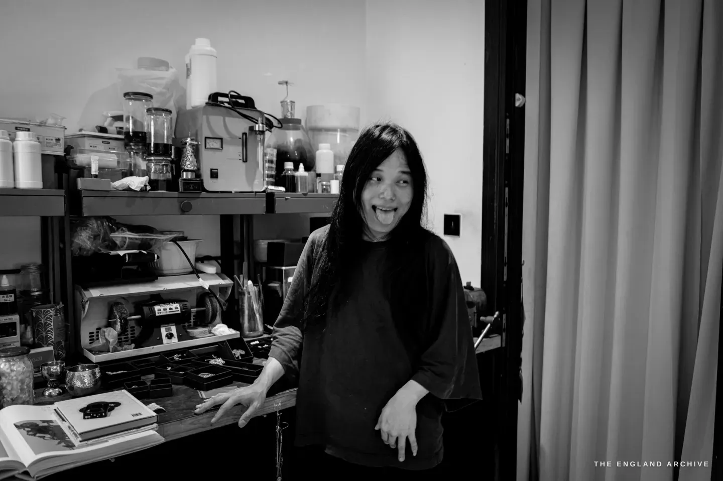 Yuyi standing by her bench, tongue out playfully, a hand on the bench edge, the chemistry shelf to one side.
