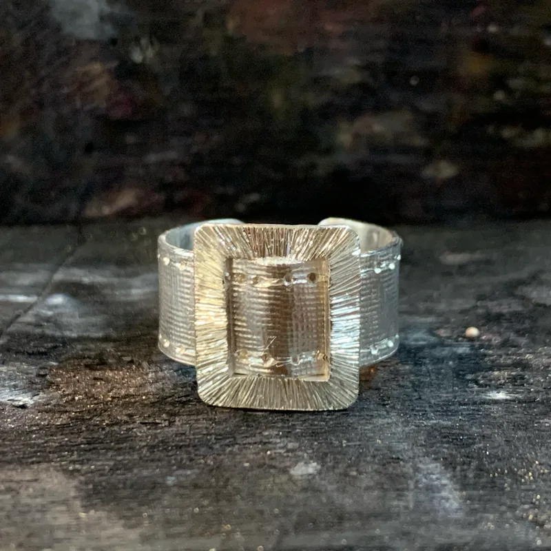 A silver ring engraved with a belt motif.