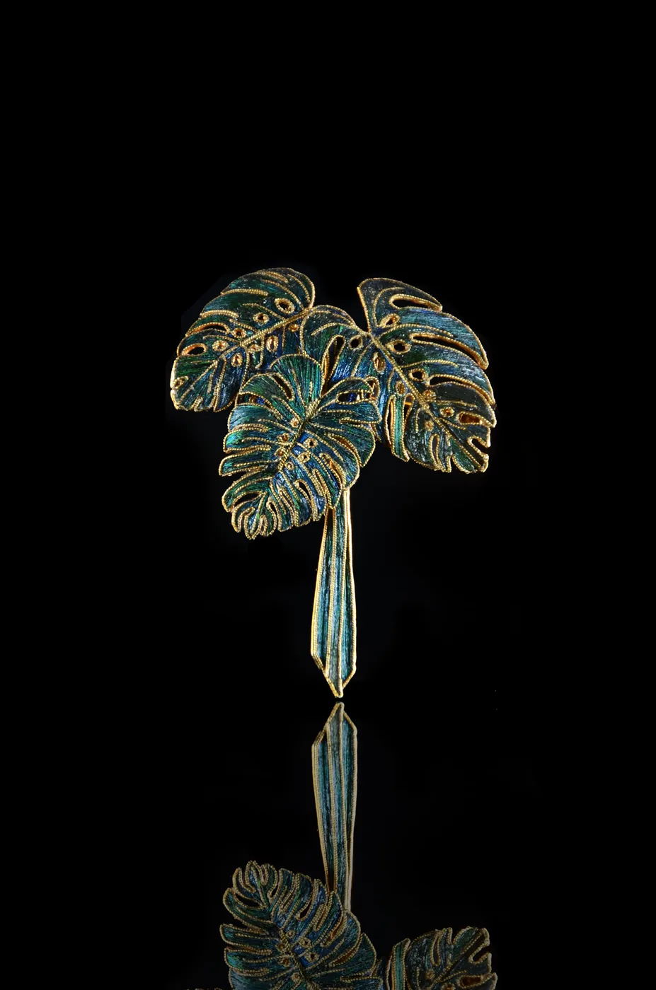 A monstera leaf brooch in green feather inlay and gold.