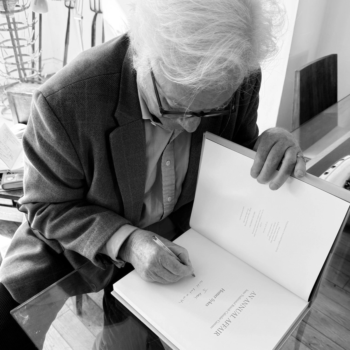 Homer Sykes signing a copy of An Annual Affair, bending over the open book with a pen in hand