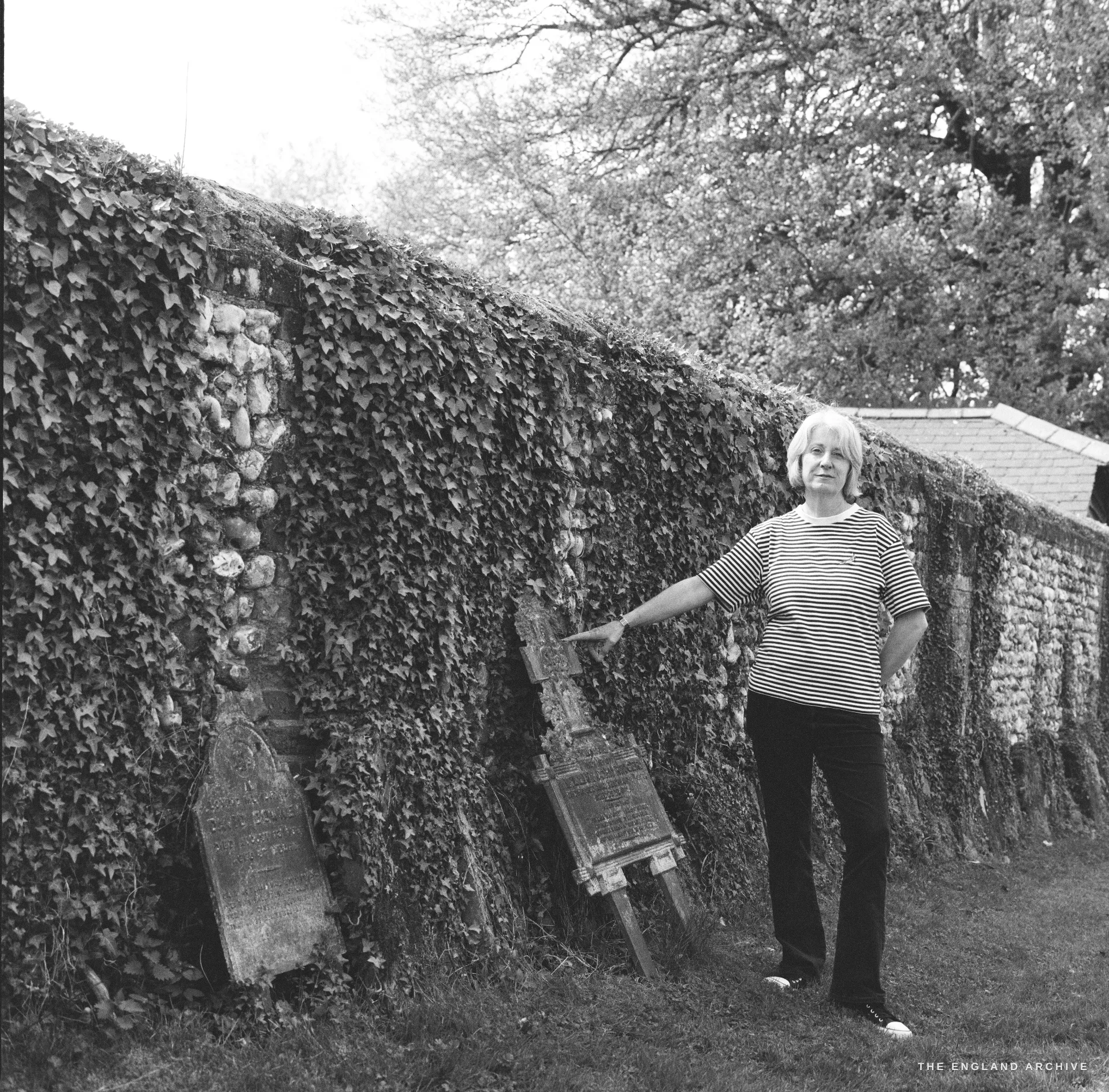 A near-identical film portrait of the same woman moments later, her hand now resting on one of the leaning gravestones.